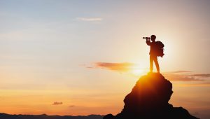 vision for success ideas. businessman's perspective for future planning. Silhouette of man holding binoculars on mountain peak against bright sunlight sky background.